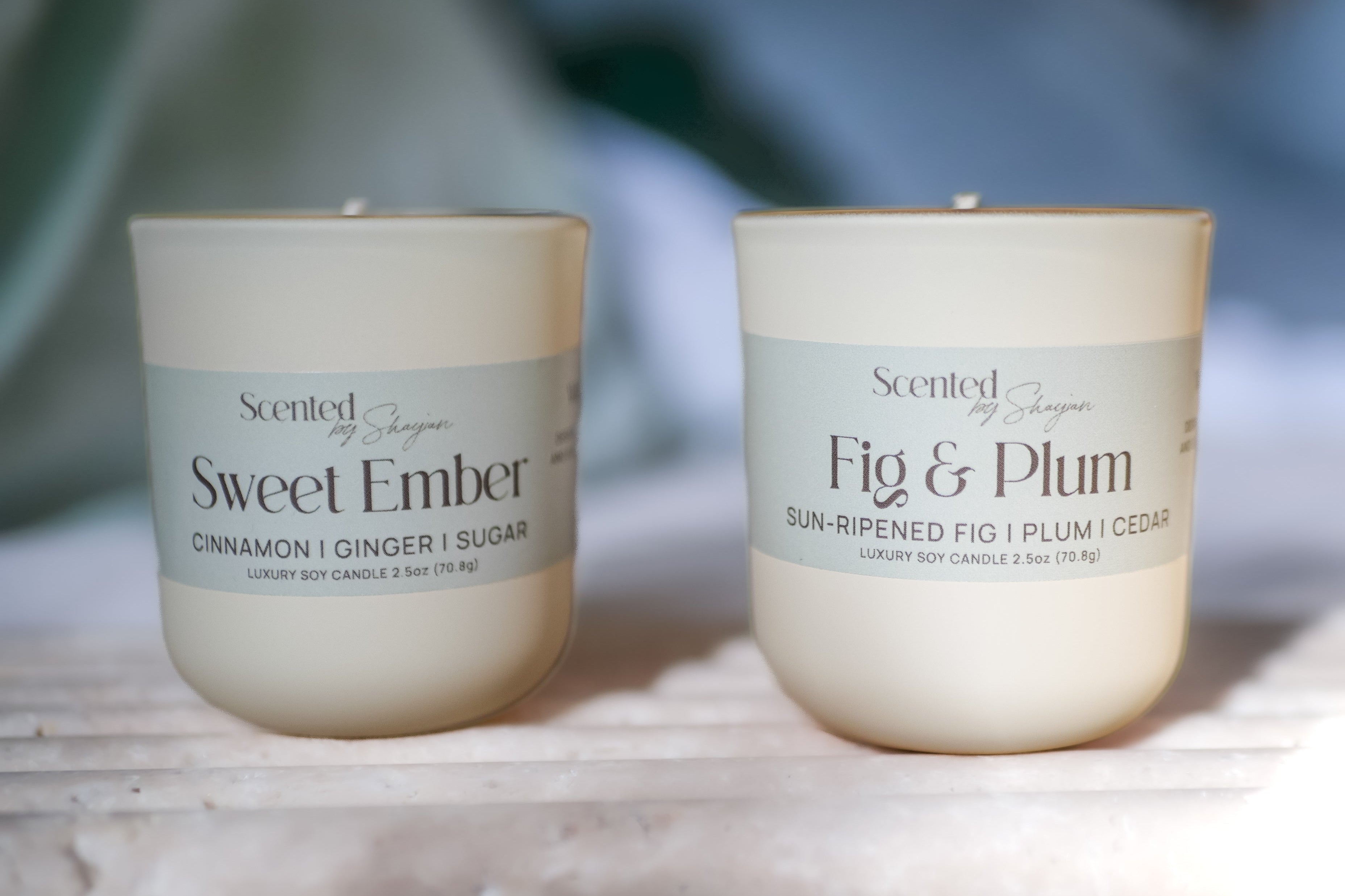 Two scented candles with labels 'Sweet Ember' and 'Fig & Plum' on a neutral background.